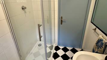 Un bagno con doccia vetrata, lavandino bianco e pavimento a scacchi.