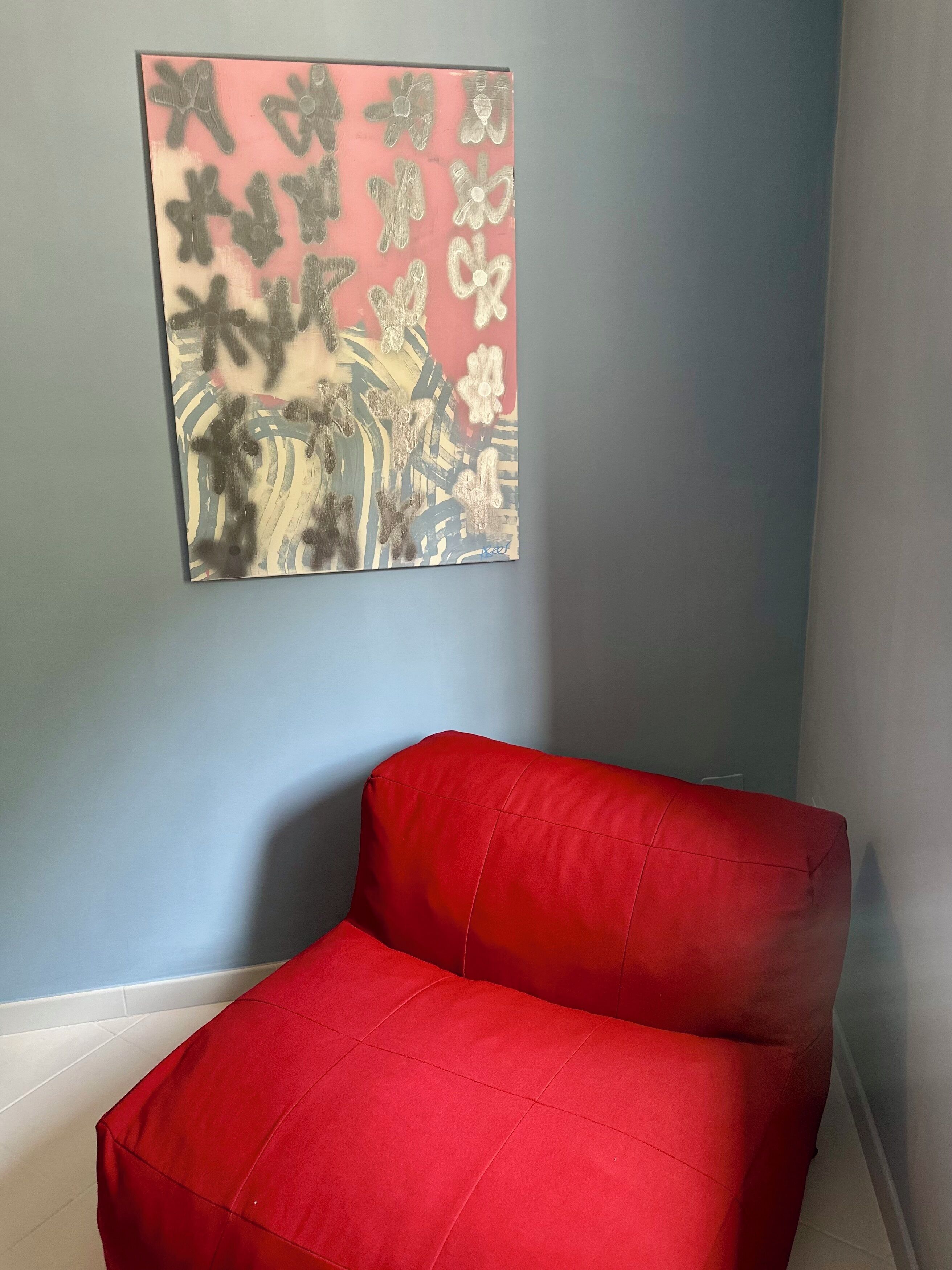 Un sillón rojo frente a una pared azul claro con un cuadro abstracto grande encima.