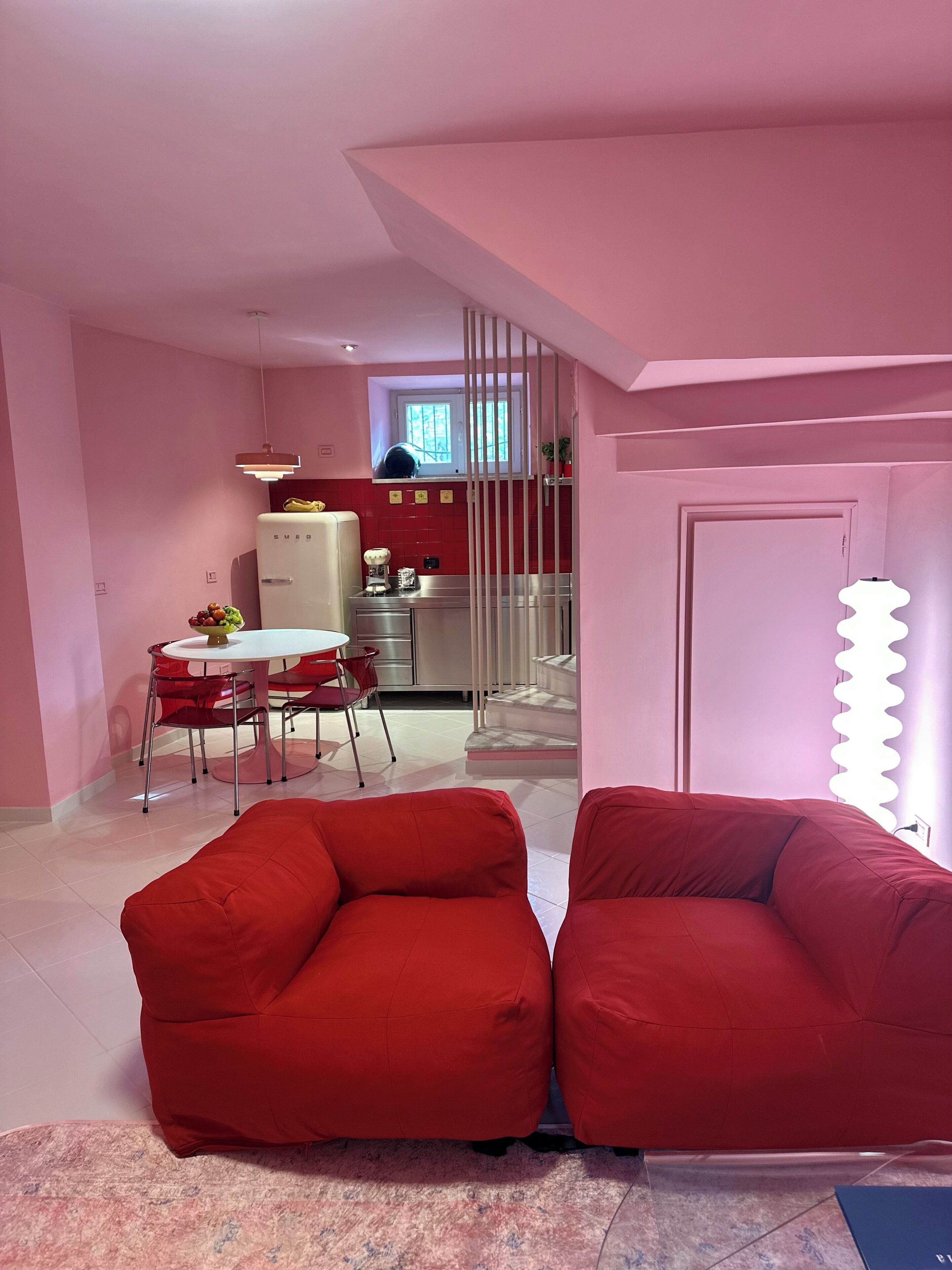 Una cucina moderna con frigorifero, piano cottura e zona pranzo con sedie rosse. In zona soggiorno ci sono due divani rossi.