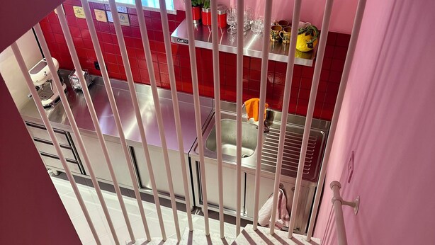 A modern kitchen with red tiles, stainless steel appliances, and a view through a barred window.