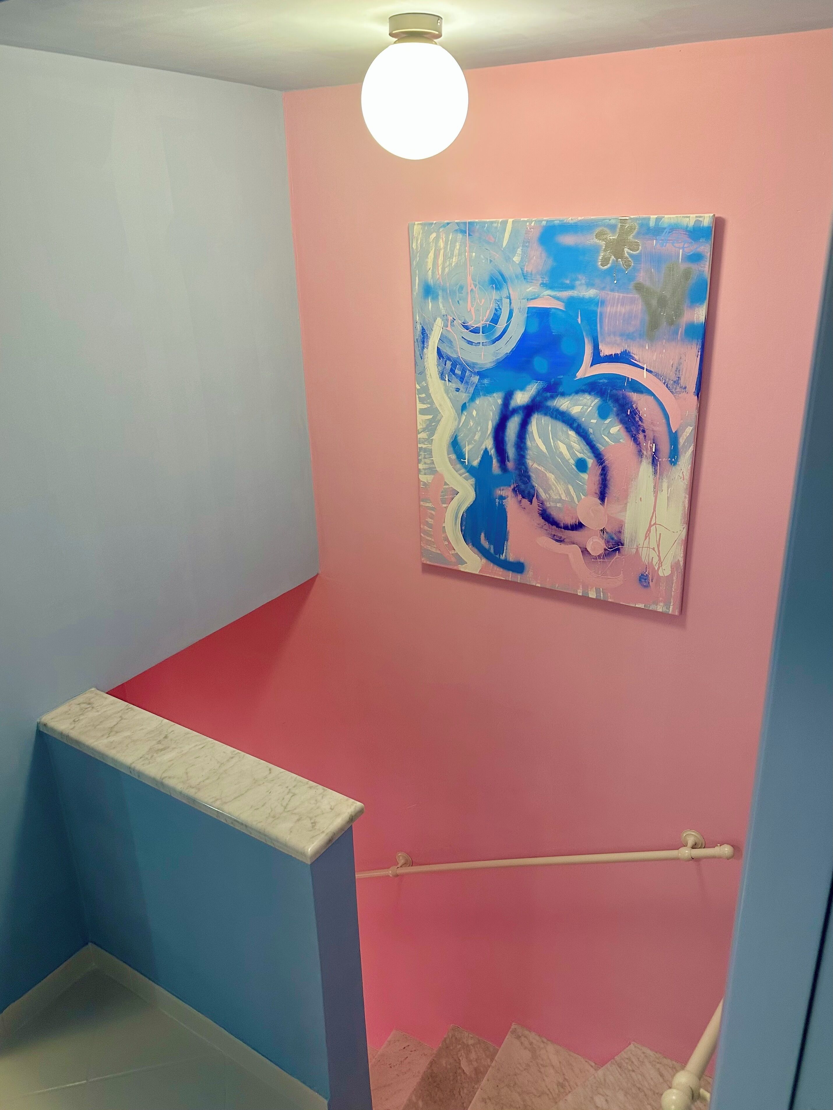 Un escalier avec un mur rouge et bleu, une corniche en marbre et un luminaire au plafond.