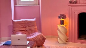 A pink-themed room with a bed, a laptop, a lamp, and a fireplace.