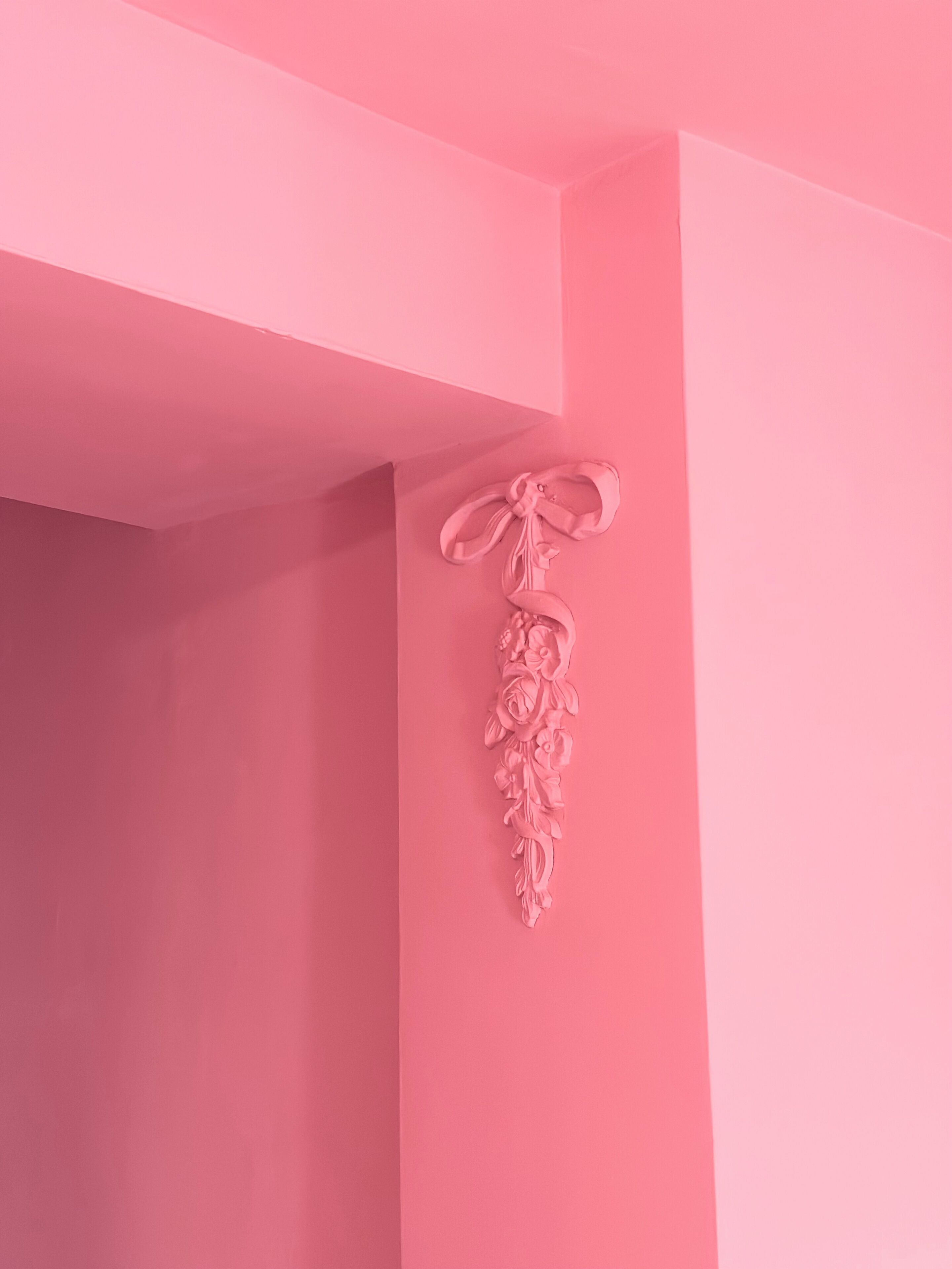 Una pared rosa con un adorno floral blanco.