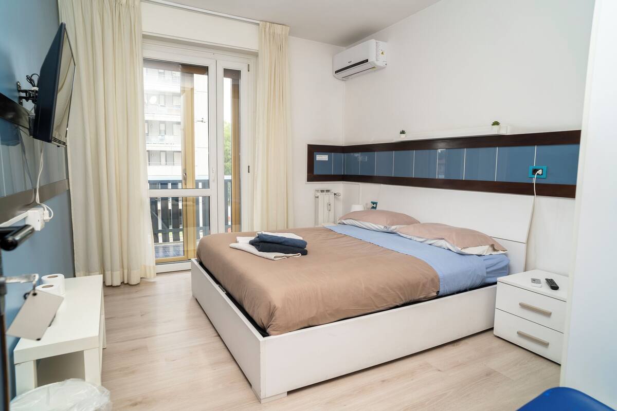 Una habitación de hotel moderna con cama, mesita de noche y vistas al balcón.
