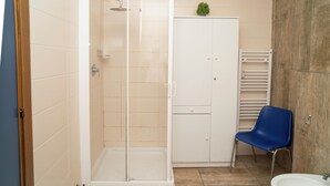 Un baño con ducha envuelta en vidrio, un mueble blanco, un sillón azul y un lavabo.