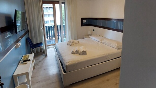 Habitación de hotel con cama, escritorio, silla, televisor y balcón.