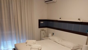 Habitación de hotel con una cama grande, mesitas de noche, un equipo de aire acondicionado y una ventana con cortinas.