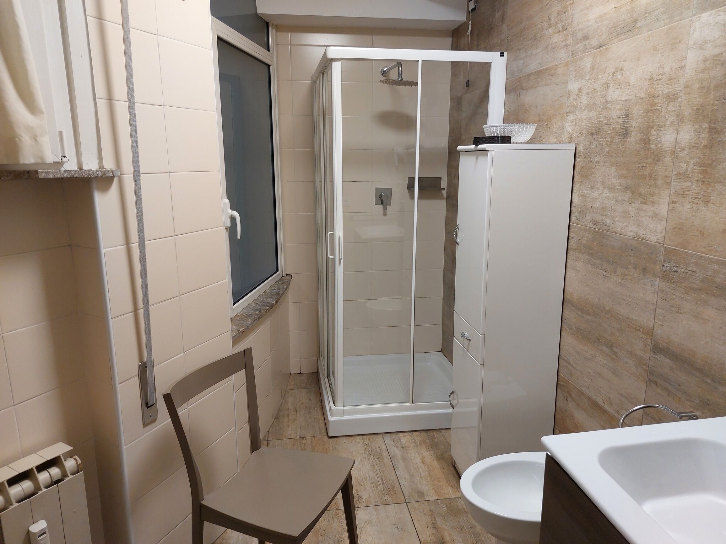 A bathroom with a shower, toilet, and a chair.