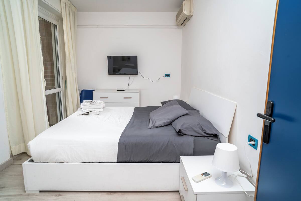 Una habitación de hotel moderna con cama, mesita de noche, lámpara y televisión en la pared.