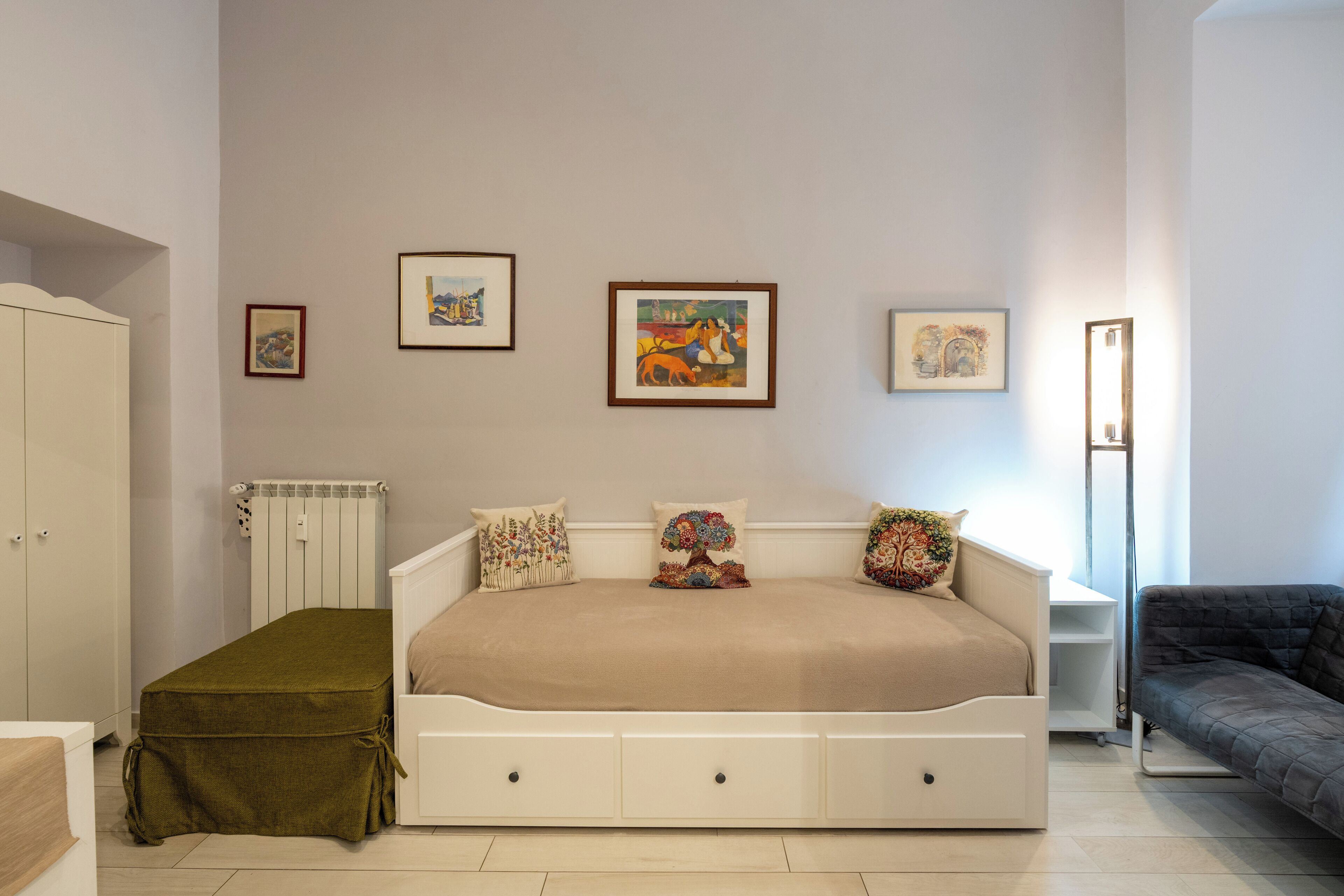 A bedroom with a bed, a bedside table, a radiator, and framed artwork on the wall.