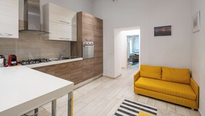 Uma cozinha moderna com armários brancos e de madeira, um fogão embutido e um sofá amarelo na sala de estar.