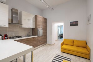 Eine moderne Küche mit weißen und hölzernen Schränken, einem eingebauten Herd und einem gelben Sofa im Wohnbereich.