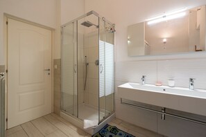 A modern bathroom with a glass-enclosed shower, a white sink with a mirror above it, and a door to the left. - A 20 Gradini dai Musei Vaticani (Rome)