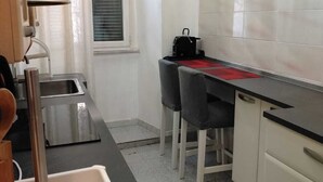 A compact kitchen with a sink, a countertop, and a window. There is a chair and a table with a red placemat. - La Casetta di Piazza Vittorio (Rome)