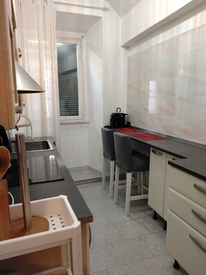 A compact kitchen with a sink, a countertop, and a window. There is a chair and a table with a red placemat. - La Casetta di Piazza Vittorio (Rome)