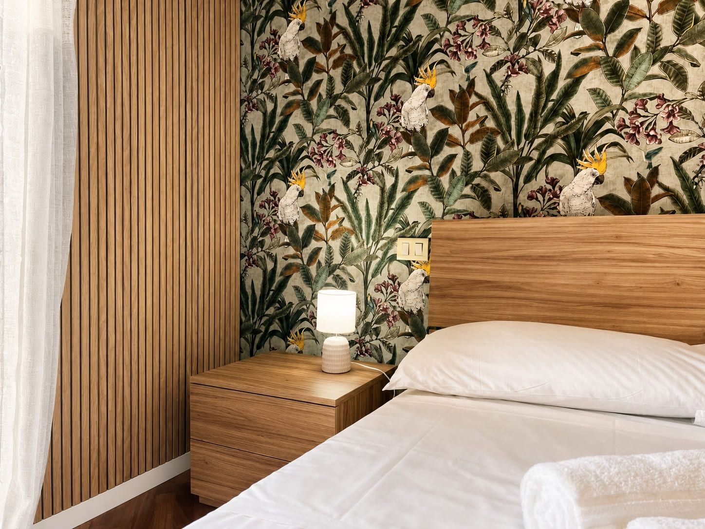 A hotel room with a wooden headboard, a bedside table with a lamp, and a floral wallpaper.