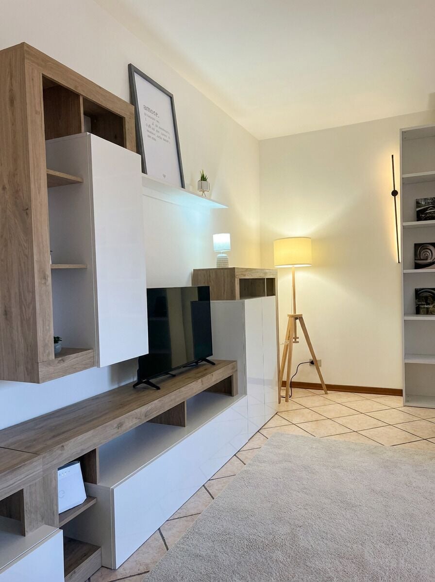 A modern living room with built-in shelving, a flat-screen TV, a standing lamp, and a bookshelf.