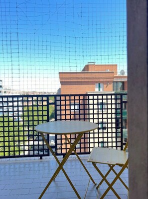 A balcony with a table and chairs, a view of buildings, and a clear sky.