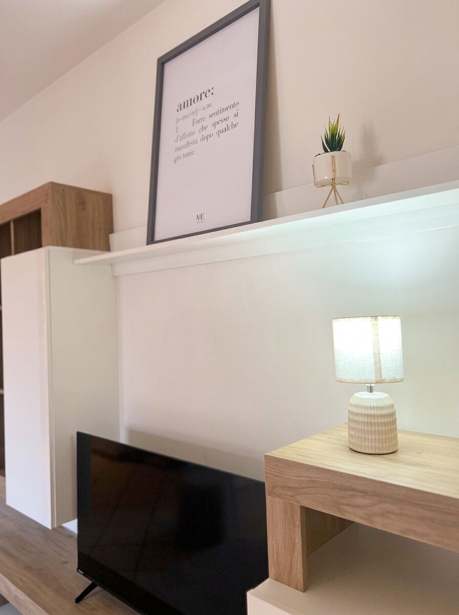 Una sala de estar moderna con una televisión de pantalla plana, una cita enmarcada en la pared, una planta pequeña en maceta y una lámpara de mesa.