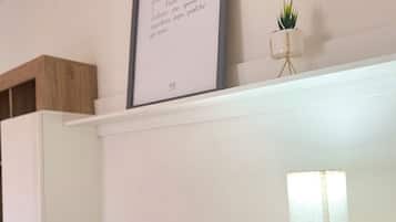 Una sala de estar moderna con una televisión de pantalla plana, una cita enmarcada en la pared, una planta pequeña en maceta y una lámpara de mesa.