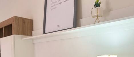 Un salon moderne avec un téléviseur à écran plat, une citation encadrée accrochée au mur, une petite plante en pot et une lampe de table.