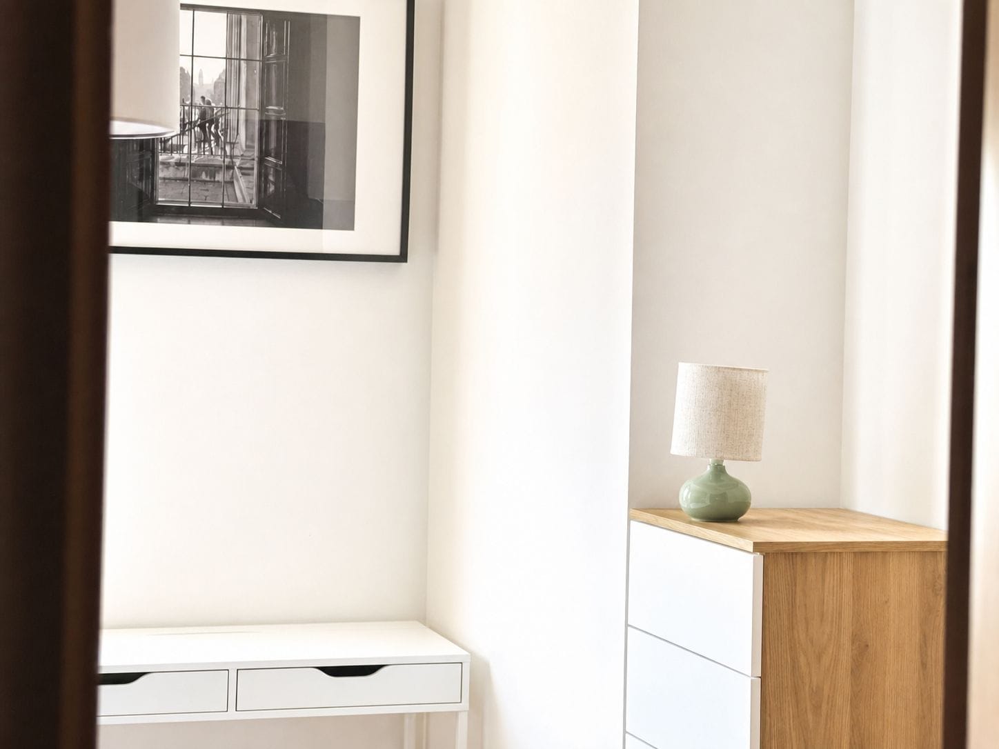 Una habitación minimalista con un escritorio blanco, un armario de madera y un cuadro en la pared.