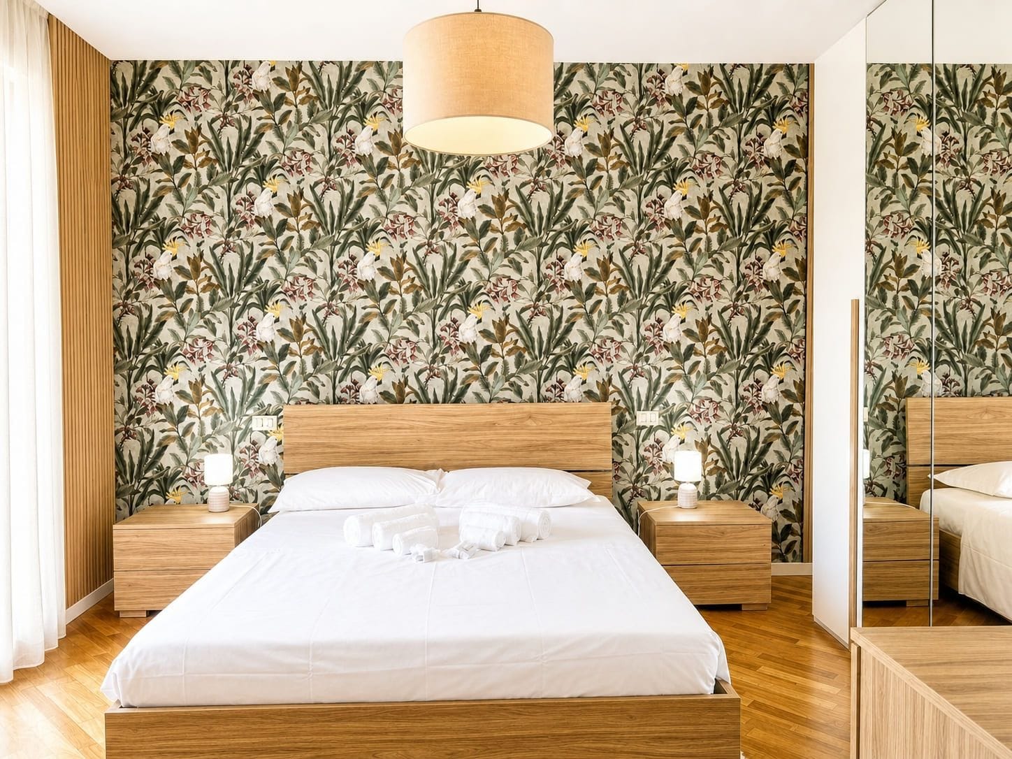 A bedroom with a large bed, wooden headboard, two bedside tables with lamps, and a floral wallpaper.