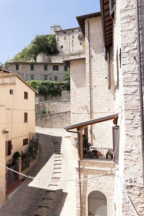 A narrow street with stone buildings, a small balcony with outdoor seating, and a tower in the background. - Dimora D'acqua e Charme (Arrone)