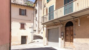 Una calle estrecha con edificios, una tienda cerrada con puerta de madera y una escalera que sube a un piso superior.