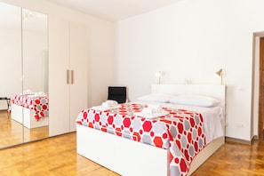 Habitación de hotel con una cama grande, un espejo, un armario y una mesita de noche con lámpara.