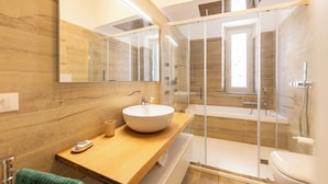 Un baño moderno con tocador de madera, un espejo grande, un lavabo blanco y una zona de ducha con mampara de cristal.