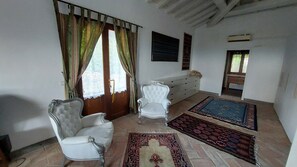 A room with a white armchair, a smaller chair, a dresser, and two rugs on the floor.
