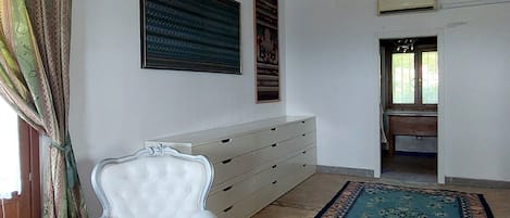 Una habitación con una butaca tapizada de blanco, un suelo con alfombra estampada, un escritorio de madera y un techo con vigas a la vista.