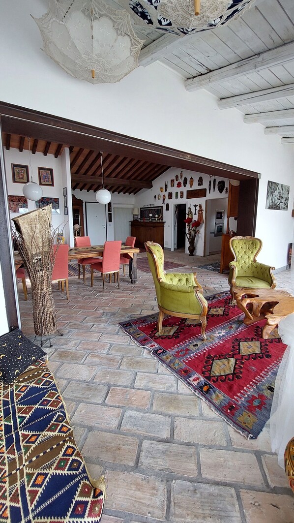 A spacious living area with a stone floor, a patterned rug, and a dining set.
