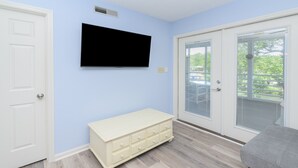 A room with a white dresser, a television mounted on the wall, and a sliding glass door leading to an outdoor area. - Walk to the Beach 2 BR Condo with a Shared Pool! Colony III 201 (Surfside Beach)