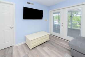 Ein Zimmer mit einem weißen Schminktisch, einem an der Wand befestigten Fernseher und einer Schiebetür zu einem Außenbereich.