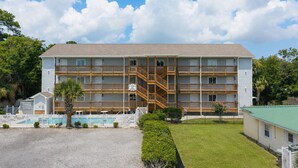 A multi-story hotel with a central staircase, a pool area, and a fenced front yard. - Walk to the Beach 2 BR Condo with a Shared Pool! Colony III 201 (Surfside Beach)