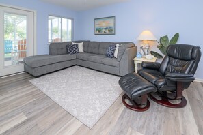 A living room with a grey sectional sofa, a black leather recliner, a patterned rug, and a painting on the wall. - Walk to the Beach 2 BR Condo with a Shared Pool! Colony III 201 (Surfside Beach)