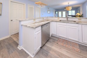 A kitchen with white cabinetry, a marble countertop, a dishwasher, and a wooden floor. - Walk to the Beach 2 BR Condo with a Shared Pool! Colony III 201 (Surfside Beach)