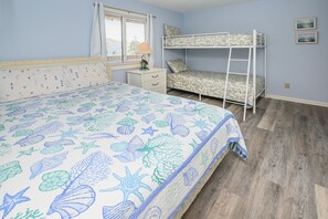 A bedroom with a bunk bed, a single bed with a patterned bedspread, a nightstand, a lamp, and two framed pictures on the wall. - Walk to the Beach 2 BR Condo with a Shared Pool! Colony III 201 (Surfside Beach)
