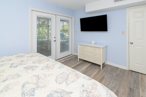 A bedroom with a bed, a dresser, a television, and a door. - Walk to the Beach 2 BR Condo with a Shared Pool! Colony III 201 (Surfside Beach)
