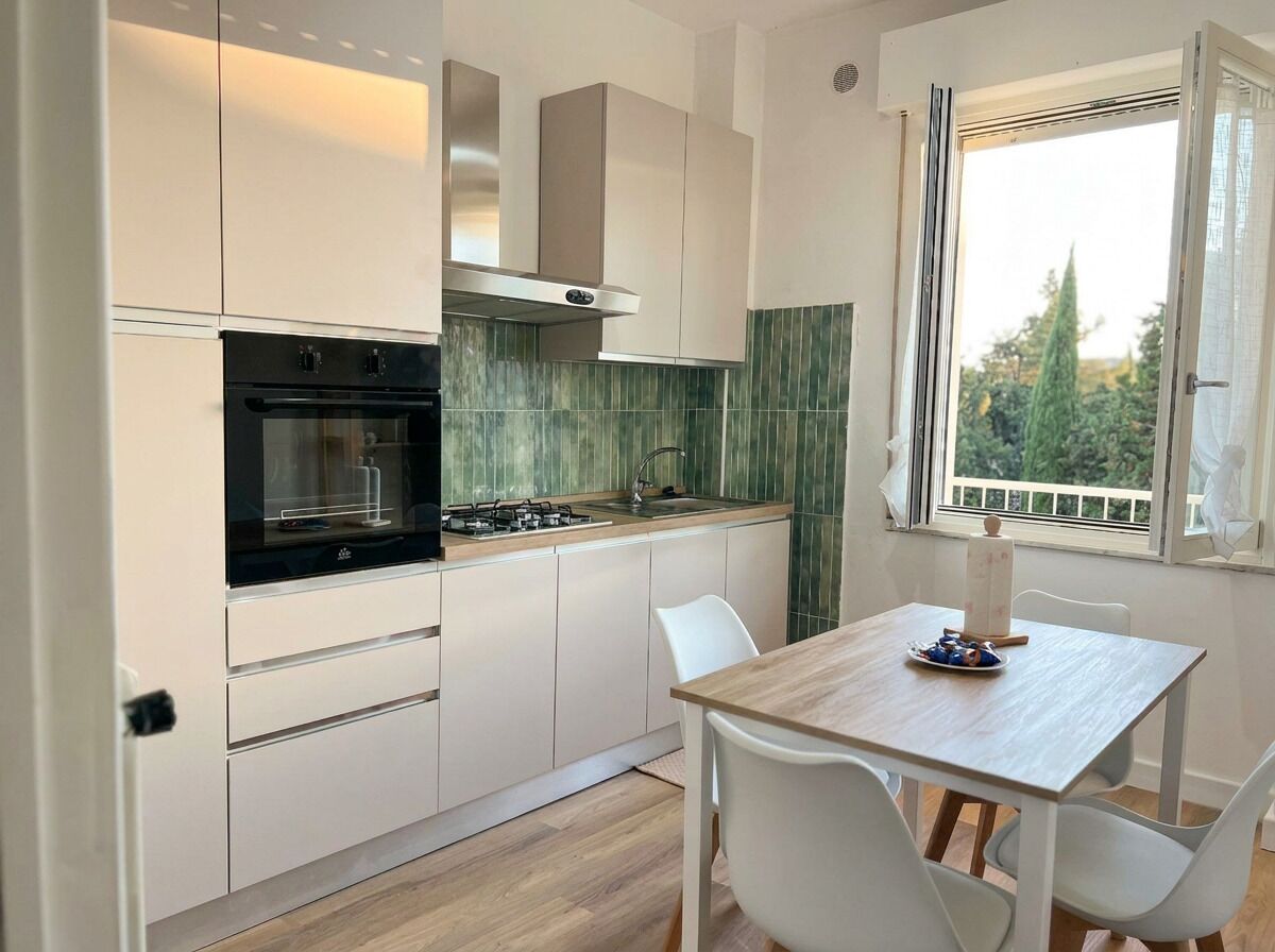 Une cuisine moderne avec des meubles blancs, un four noir et une table à manger en bois, assortie de chaises blanches.