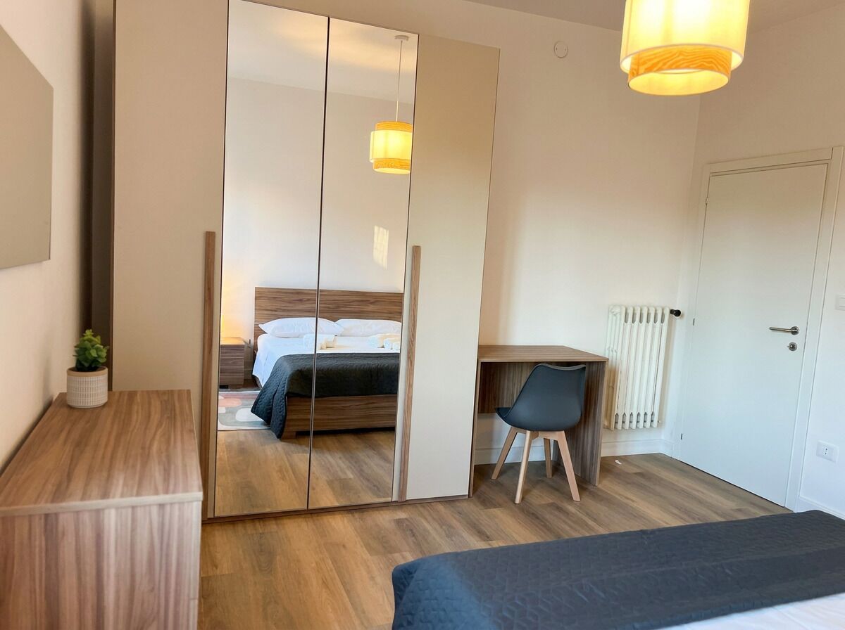 A bedroom with a bed, a desk, a chair, a wardrobe, and a bedside lamp.