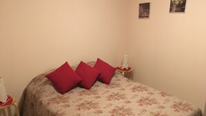 Ein Bett mit floralem Überwurf und drei roten Kissen. Zwei Nachttische mit weißen Lampen stehen daneben.