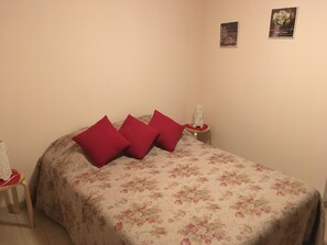 A bed with a floral bedspread and three red pillows. There are two bedside tables with white lamps. - Apartment 'La Maison Des Bains De César' with Mountain View and Wi-Fi (Mont-Dore)