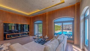 A modern living room with a large sofa, a flat-screen TV, and a dining table.