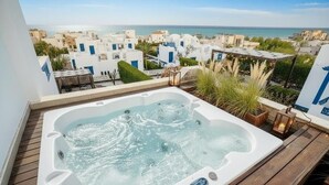 A hot tub on a wooden deck with a view of a coastal town.