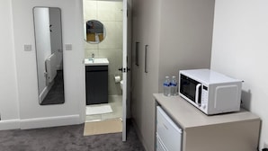 A compact hotel room with a kitchenette, a mirror, a door leading to a bathroom, and a microwave on a small table. - London Harrow Hotel (Harrow)