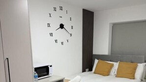 A hotel room with a bed, a bedside table with a microwave, a small refrigerator, and a wall clock. - London Harrow Hotel (Harrow)