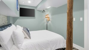 Ein Schlafzimmer mit einem Bett, Kissen, einem an der Wand montierten Fernseher und einer Stehlampe.